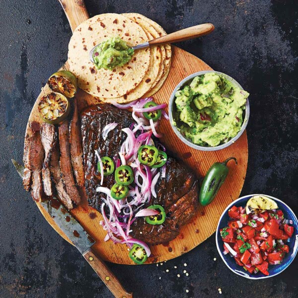 The makings of beef fajitas on a wooden board - tortillas, steak, guacamole, salsa.