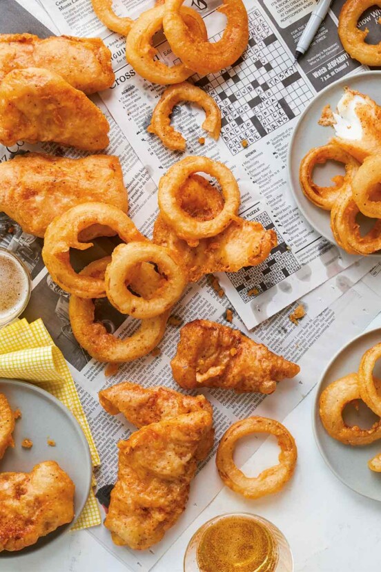 Several pieces of beer-battered fish scattered across newspaper with fried onions rings and two glasses of beer.