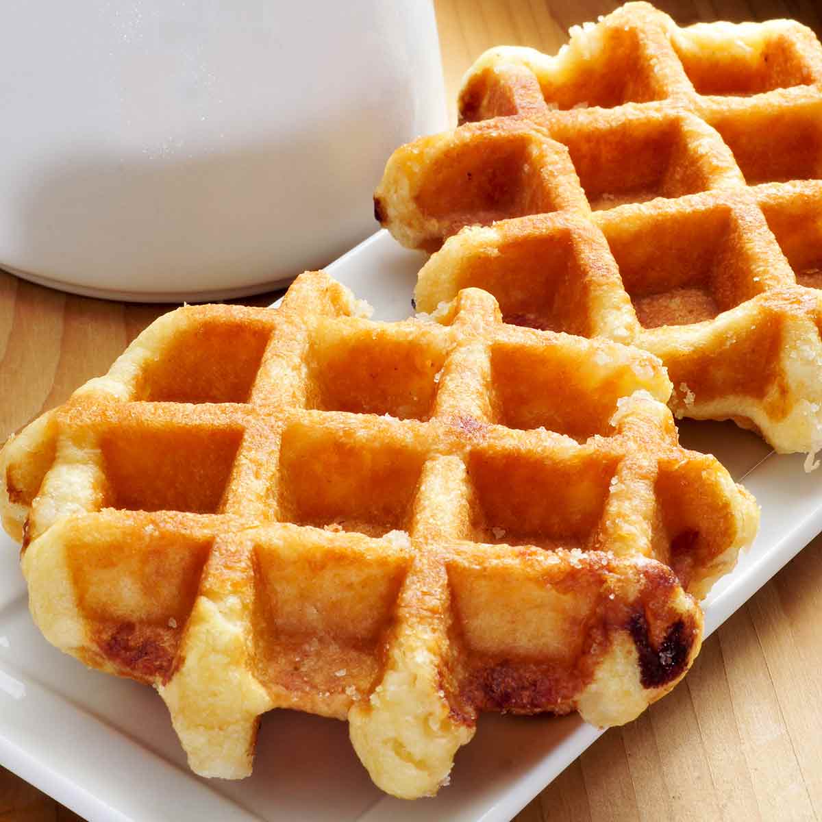 Belgian Liege waffles divided between plates with a pitcher of cream in the background.