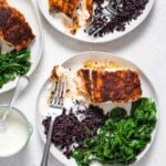 Three white plates with blackened red snapper, black rice, yogurt sauce, and sauteed spinach.