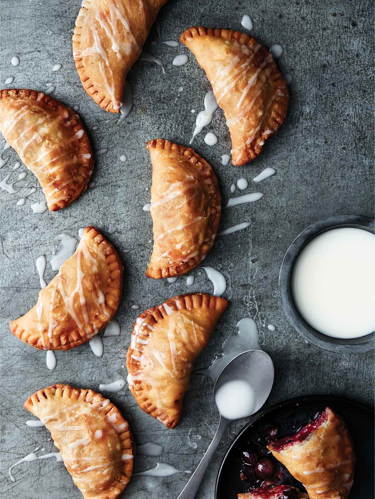 8 crescent-shape blueberry fried pies with Meyer lemon drizzle sauce nearby all on a piece of slate