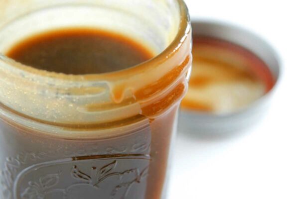 A small jar filled with butterscotch sauce with some dripping down the side and a lid in the background.