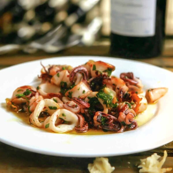 A white plate topped with calamari à la plancha -- seared calamari -- with a bottle of wine in the background.