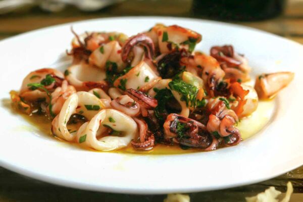 A white plate topped with calamari à la plancha -- seared calamari -- with a bottle of wine in the background.