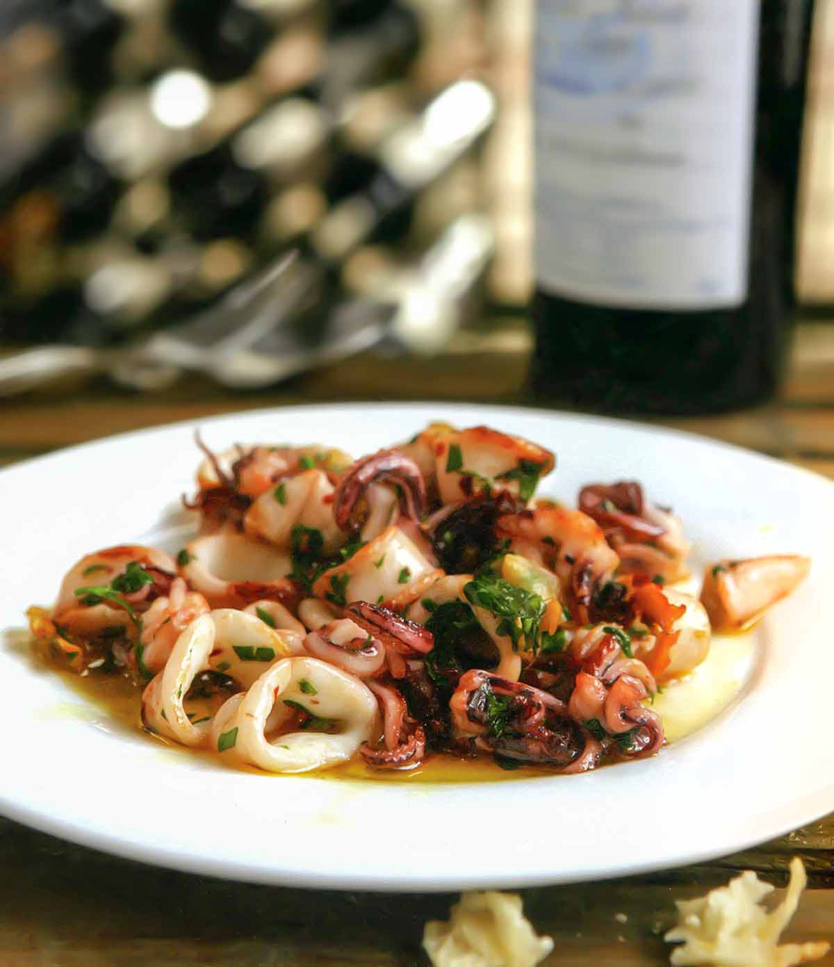 A white plate topped with calamari à la plancha -- seared calamari -- with a bottle of wine in the background.