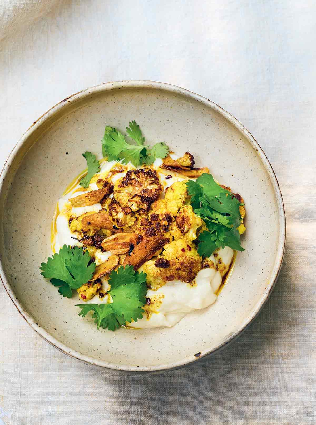 A ceramic shallow bowl filled with cauliflower puree with garlic and spices and roasted cauliflower and cilantro on top.
