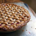 A whole cherry pie with a lattice crust on a baking sheet on a wood table.