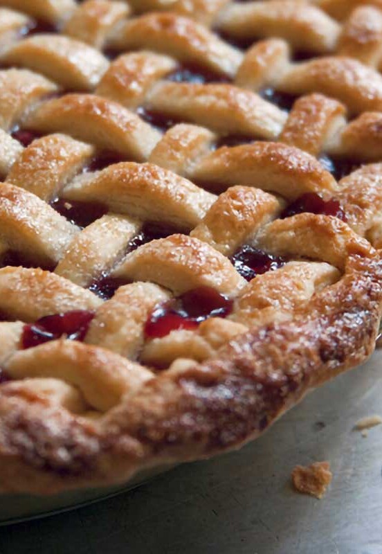 A whole cherry pie with a lattice crust on a baking sheet on a wood table.