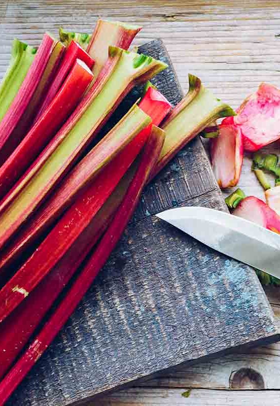 Stalks of rhubarb on a cutting board with ends trimmed and a knife beside them.