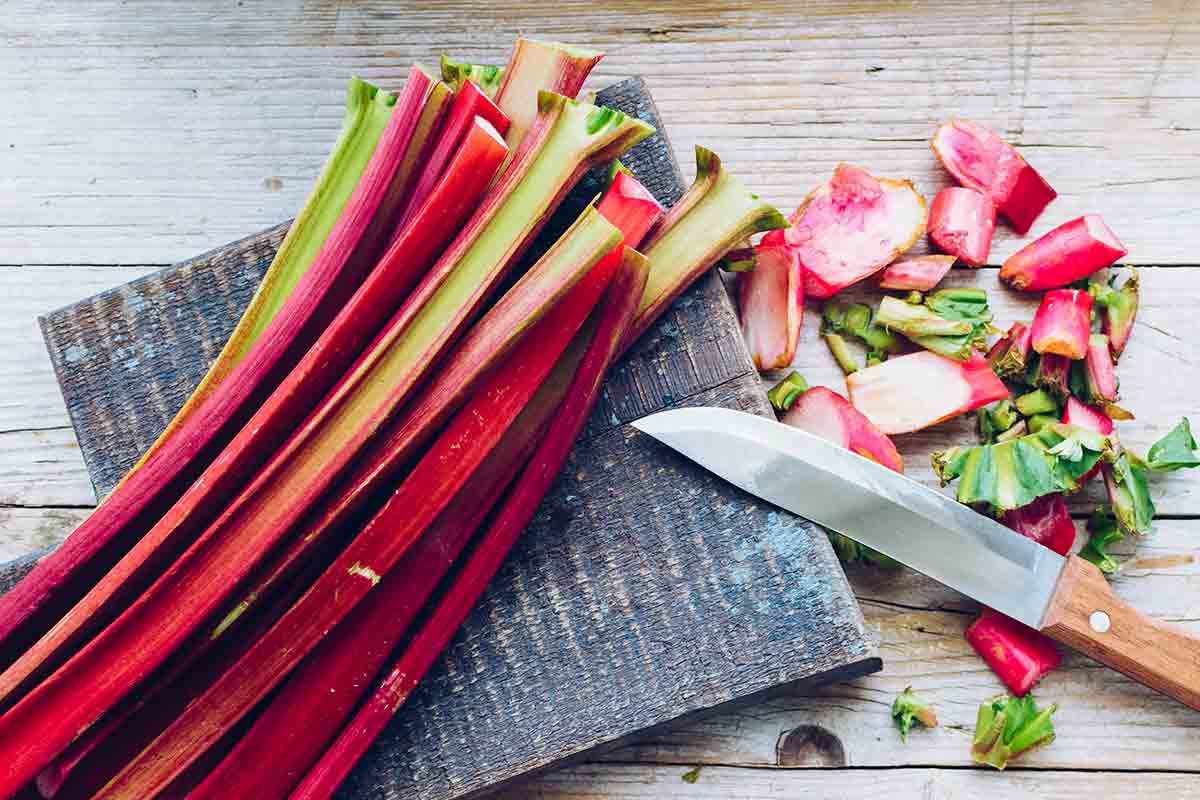 Stalks of rhubarb on a cutting board with ends trimmed and a knife beside them.