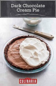 A dark chocolate cream pie partially covered with whipped cream and a knife and a bowl of whipped cream on the side.