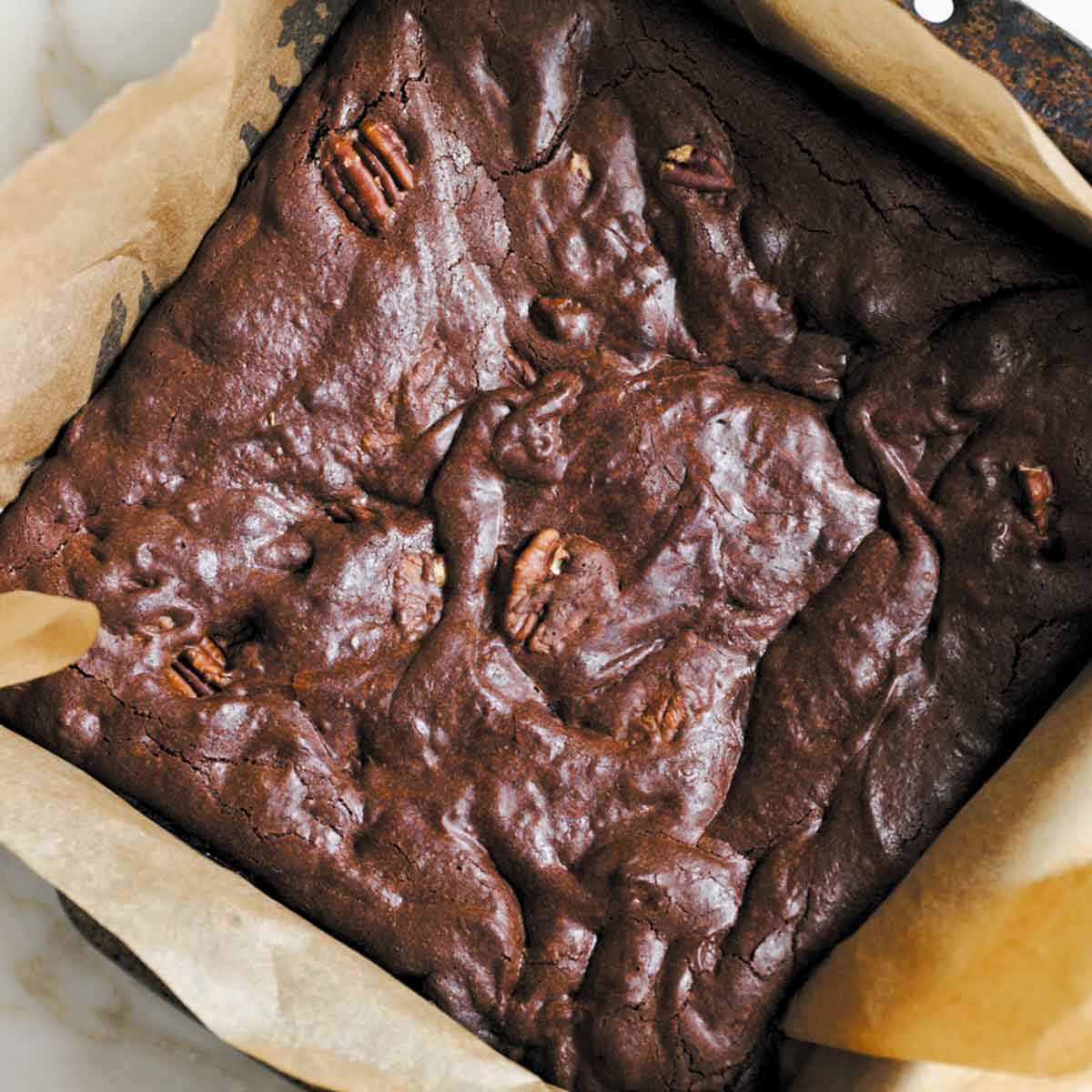 A parchment-lined square pan filled with pecan-studded best brownies.