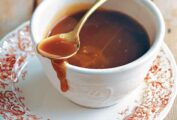 A cup of easy caramel sauce on a saucer with a spoon resting on top.