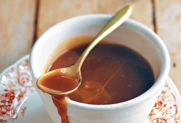 A cup of easy caramel sauce on a saucer with a spoon resting on top.