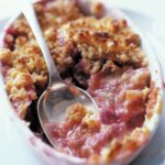 A white baking dish filled with easy rhubarb crisp and a spoon resting in the center.