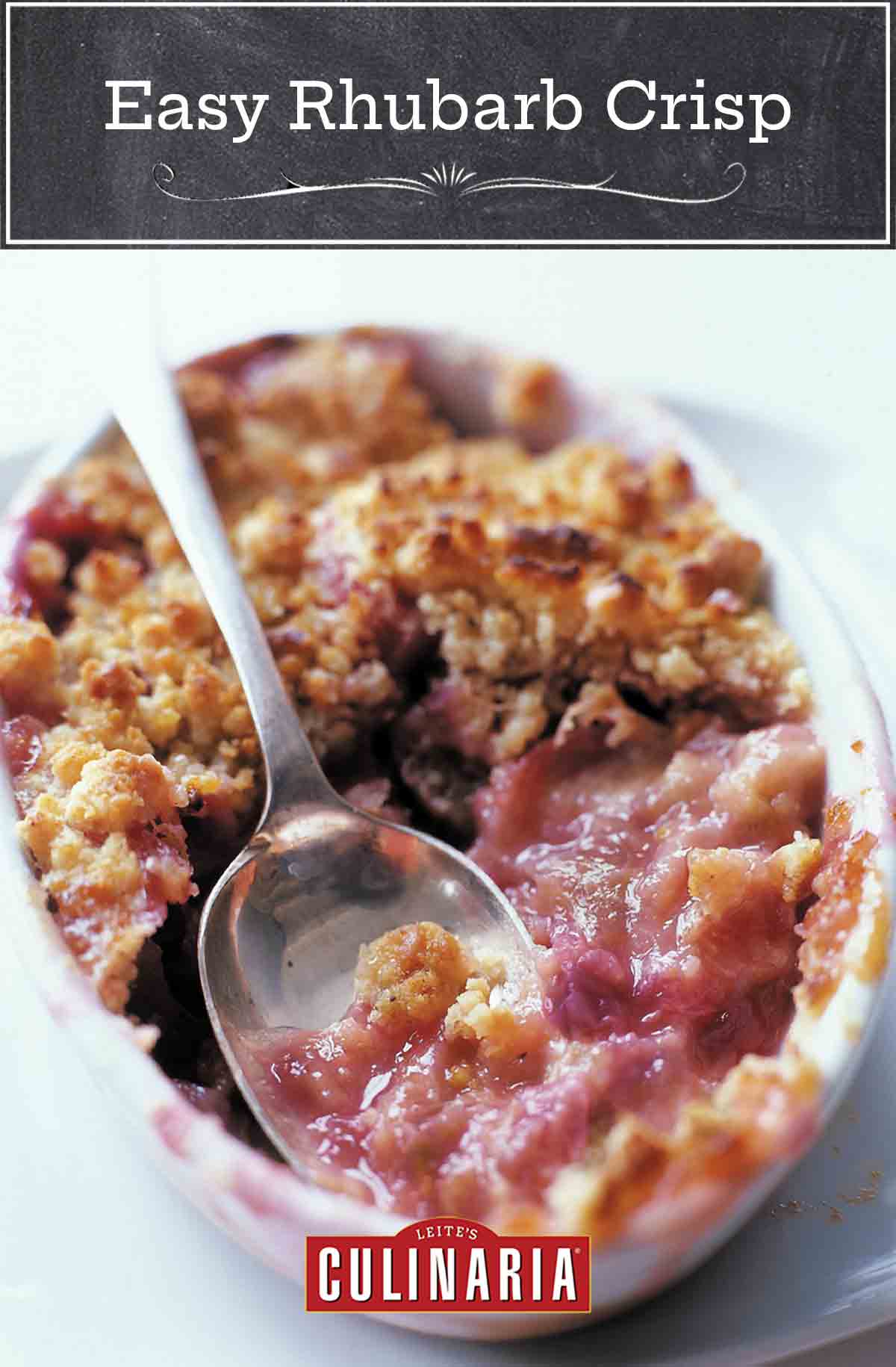 A white baking dish filled with easy rhubarb crisp and a spoon resting in the center.