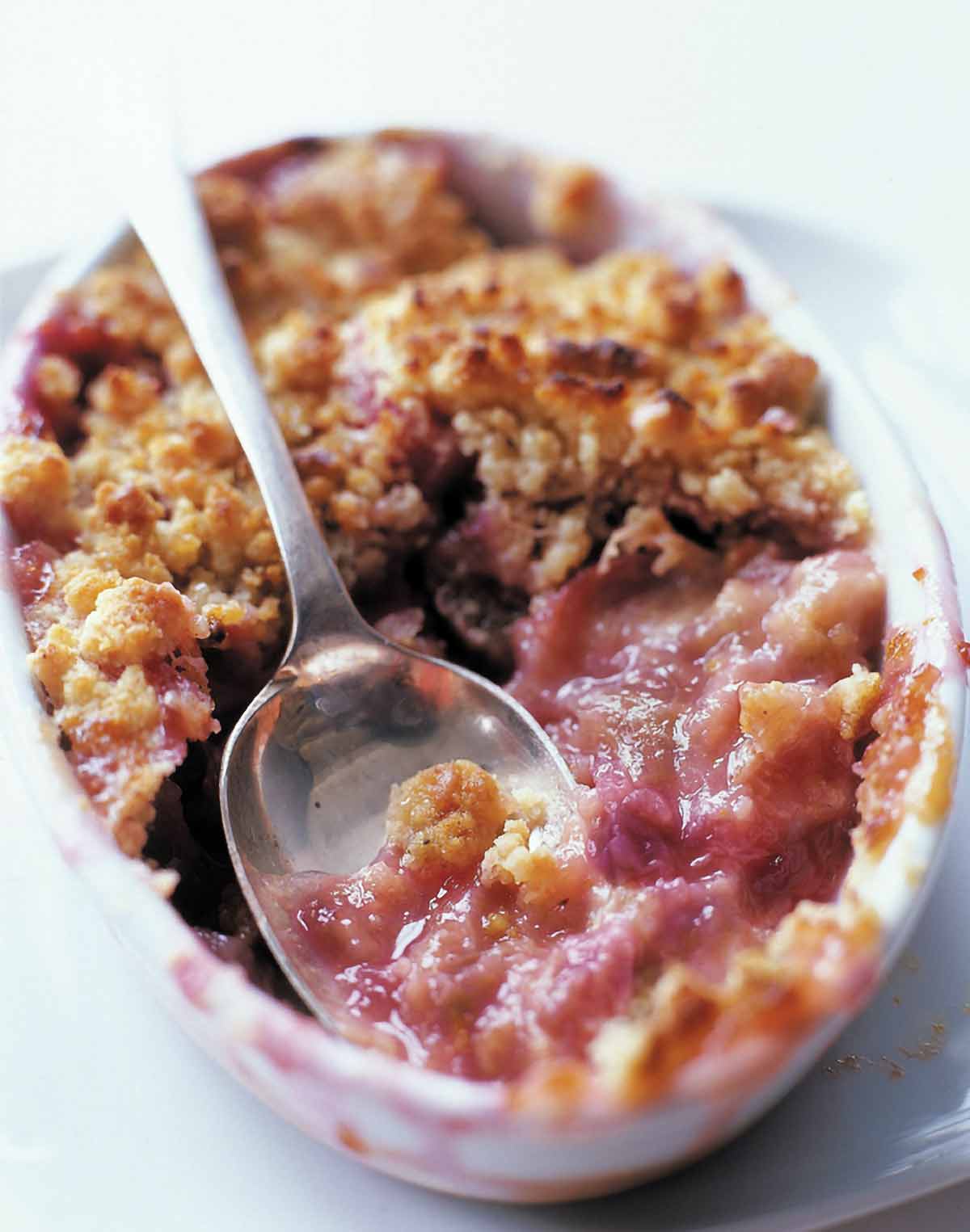 A white baking dish filled with easy rhubarb crisp and a spoon resting in the center.