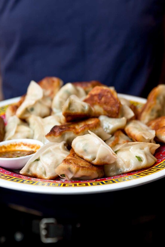 A person holding a platter of fried pork dumplings and bowl of dipping sauce.