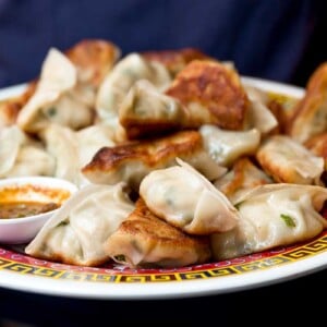 A person holding a platter of fried pork dumplings and bowl of dipping sauce.