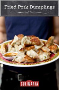 A person holding a platter of fried pork dumplings and bowl of dipping sauce.