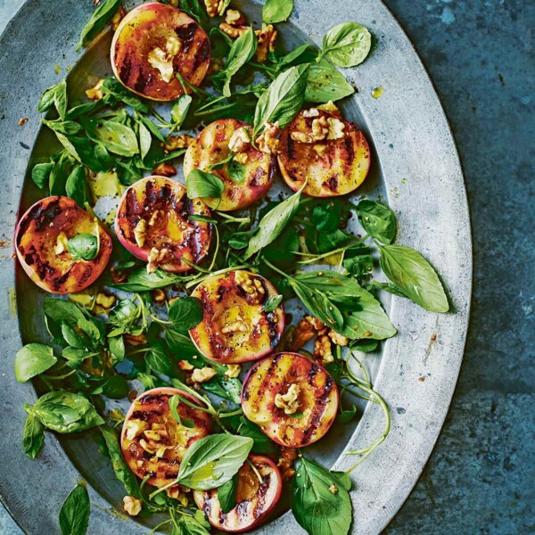 An oval platter topped with grilled peach, basil, and walnut salad