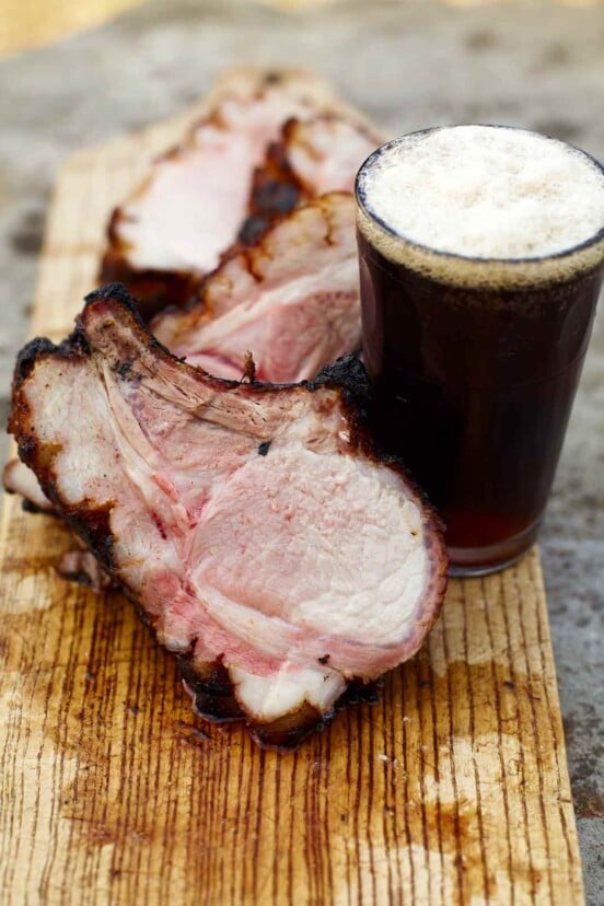 Chops from a spice-glazed grilled pork loin on a cutting board with a glass of stout.
