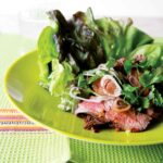 A grilled Thai beef salad with lettuce, thinly sliced beef, shallots, and cilantro, on a green plate.