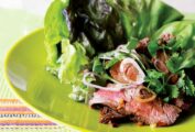 A grilled Thai beef salad with lettuce, thinly sliced beef, shallots, and cilantro, on a green plate.