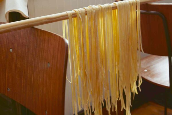 Homemade tagliatelle hanging over a broomstick resting on the back of two chairs.