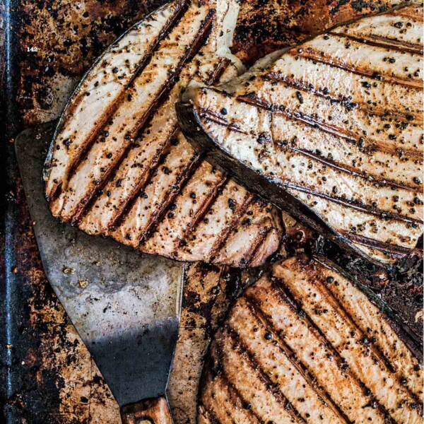 Several grilled fish fillets on a baking sheet with a spatula underneath them.