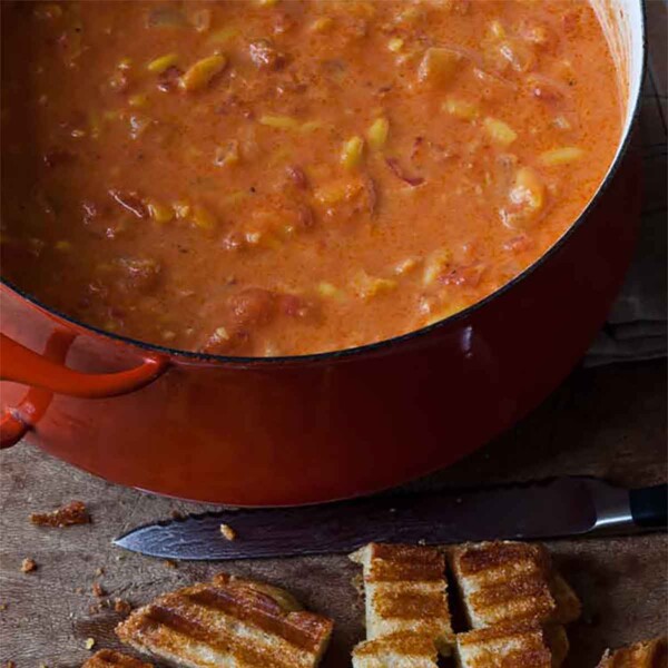 A large pot of Ina Garten's easy tomato soup with a grilled cheese sandwich being cut into croutons beside it.