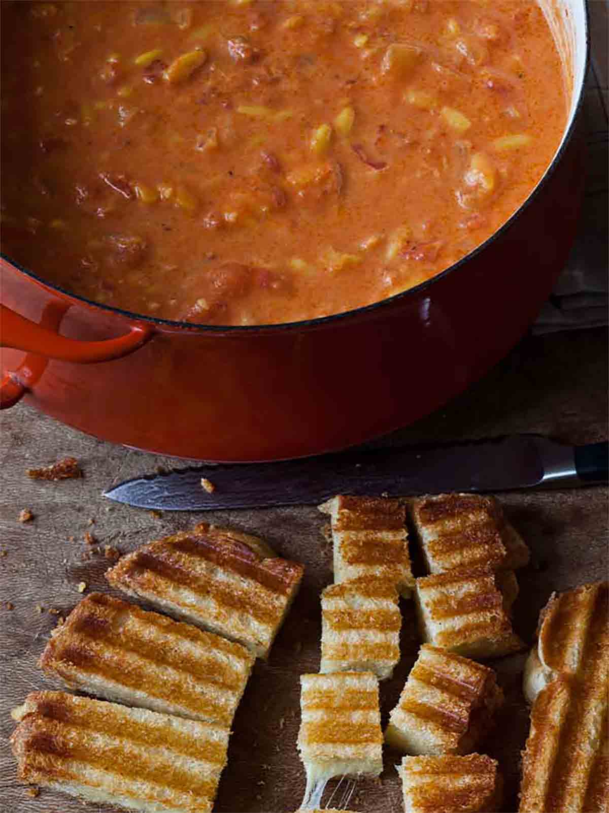 A large pot of Ina Garten's easy tomato soup with a grilled cheese sandwich being cut into croutons beside it.