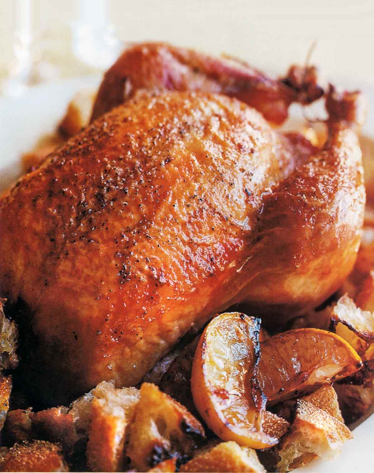 Ina Garten's lemon chicken roasted on top of a bed of bread croutons and lemon wedges.