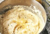 A saucepan filled with Ina Garten's mashed potatoes with lemon and black pepper and a whole lemon and zester next to it.