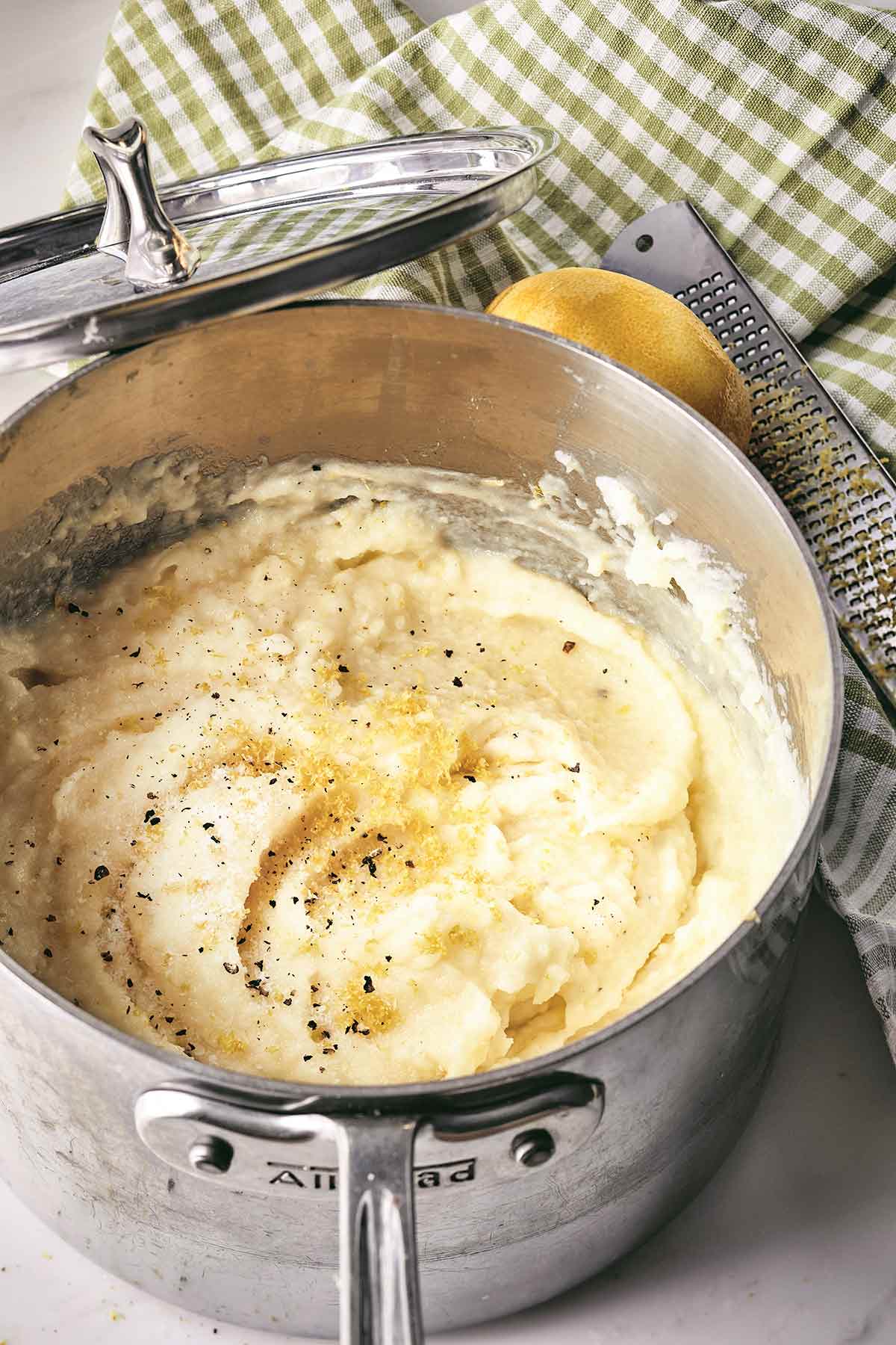 A saucepan filled with Ina Garten's mashed potatoes with lemon and black pepper and a whole lemon and zester next to it.