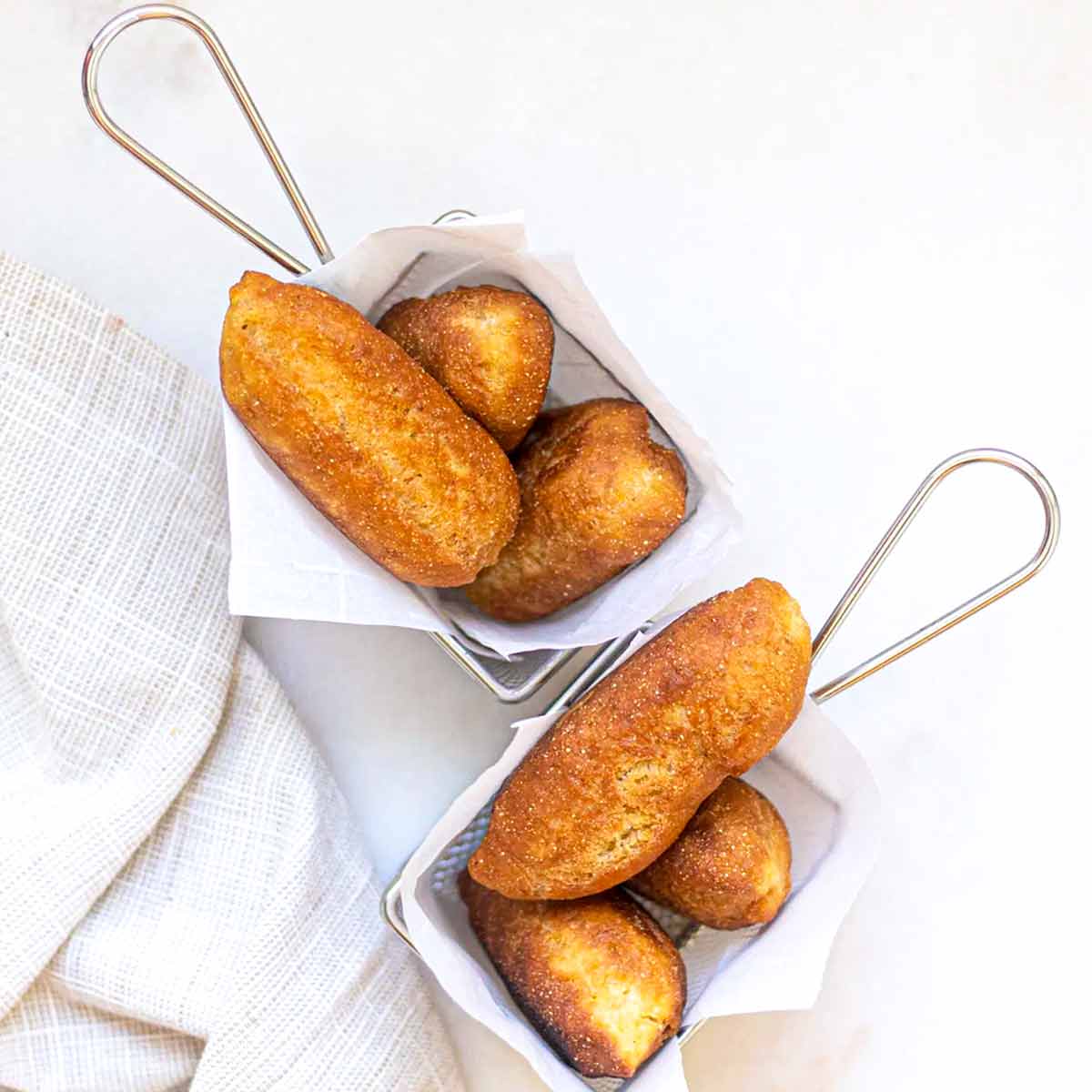 Two metal baskets lined with paper, each with three Jamaican fried dough fritters, or festival.