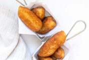 Two metal baskets lined with paper, each with three Jamaican fried dough fritters, or festival.