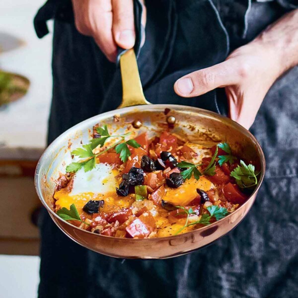 A person holding a skillet with jazmaz, or Syrian shakshuka - eggs cooked in a tomato and chile sauce.