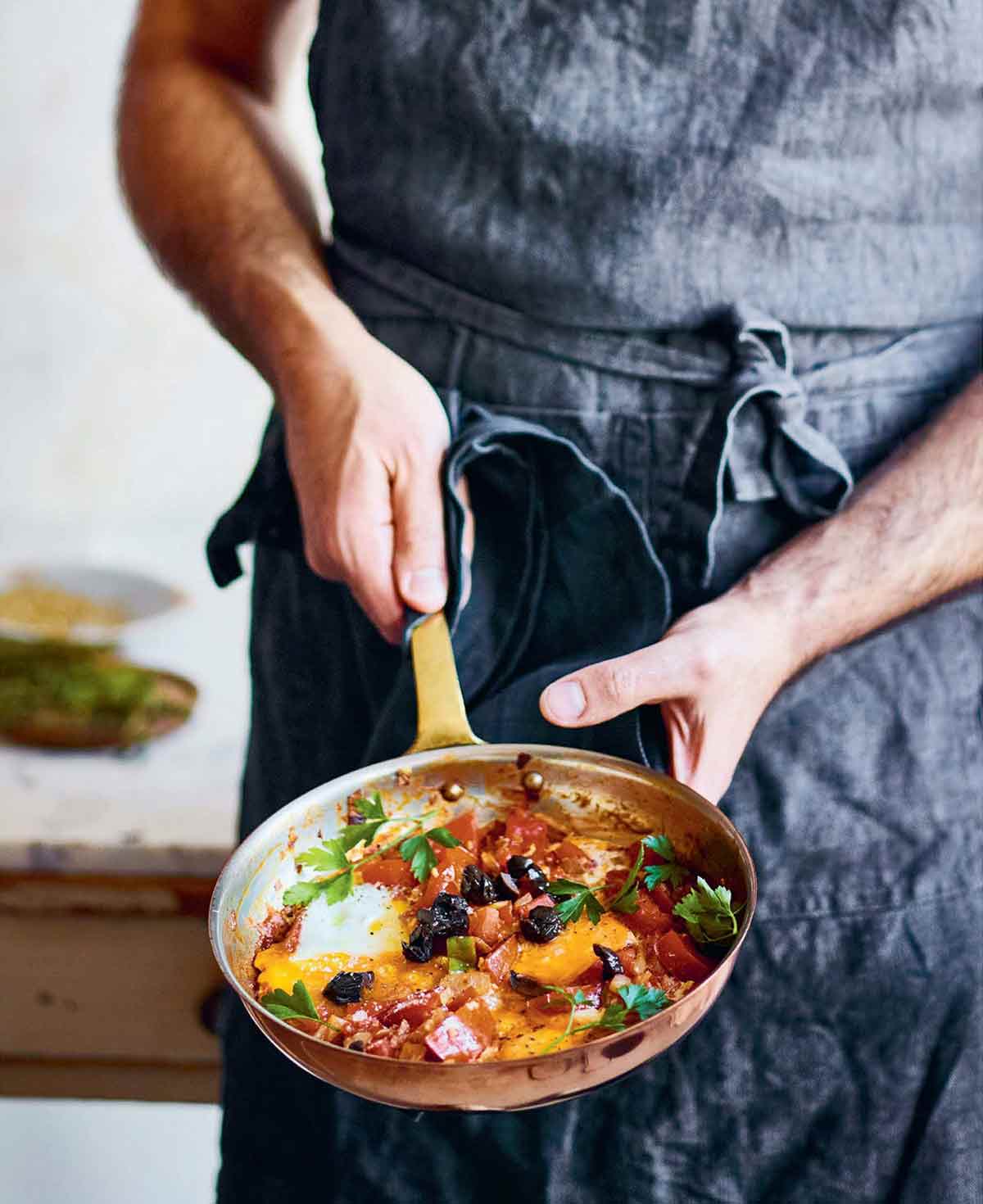 En person som håller i en stekpanna med jazmaz, eller syrisk shakshuka - ägg kokta i en tomat- och chilisås.