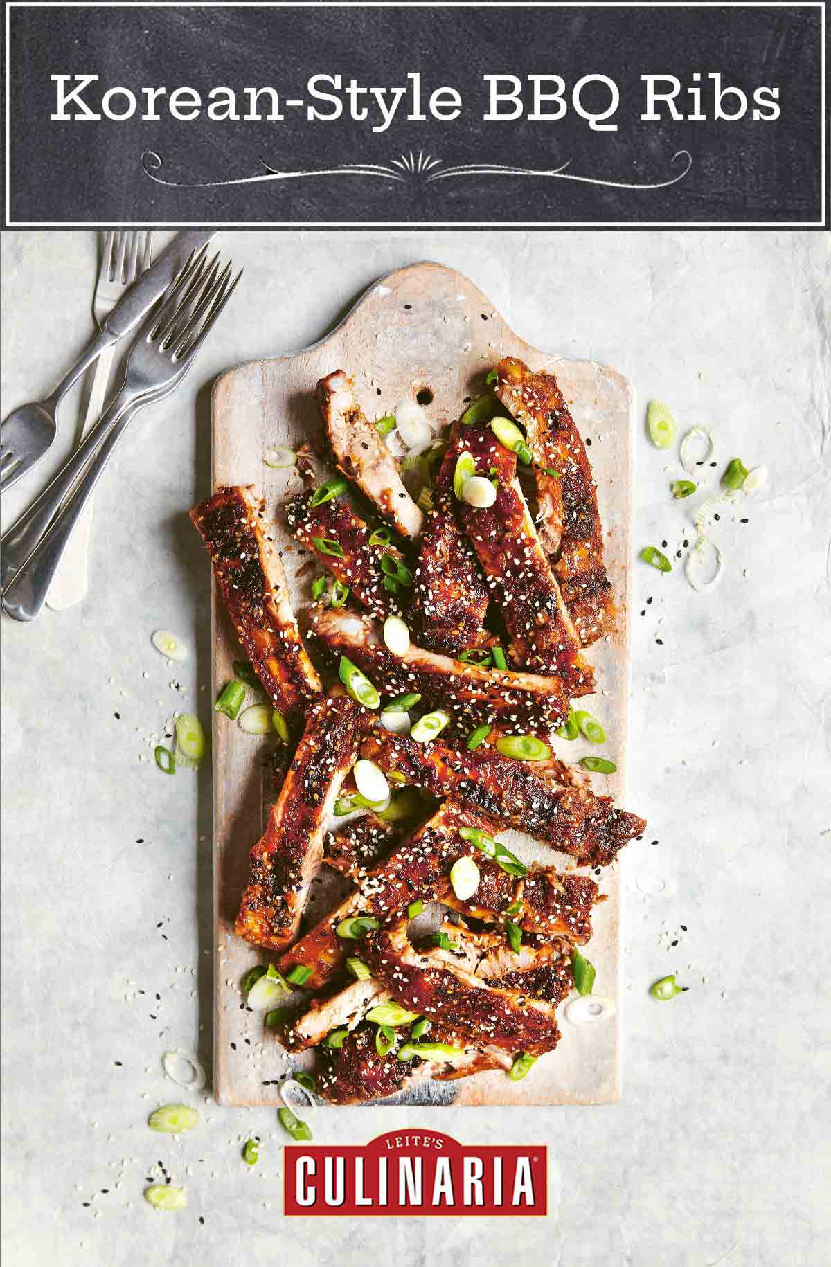 A pile of Korean-style BBQ ribs on a wooden board, garnished with scallions and sesame seeds with several forks on the side.