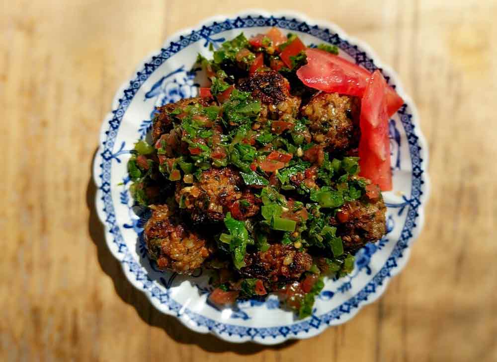 A blue and white plate filled with lamb kofte and parsley and tomato salad.
