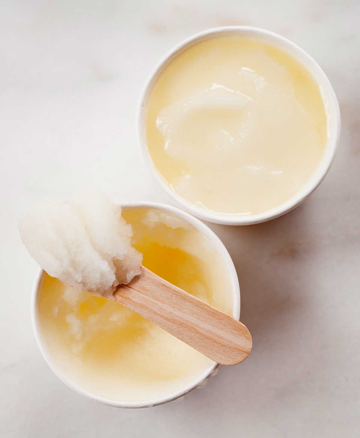 Two small bowls of lemon ice, with a wooden popsicle stick resting on top of one.