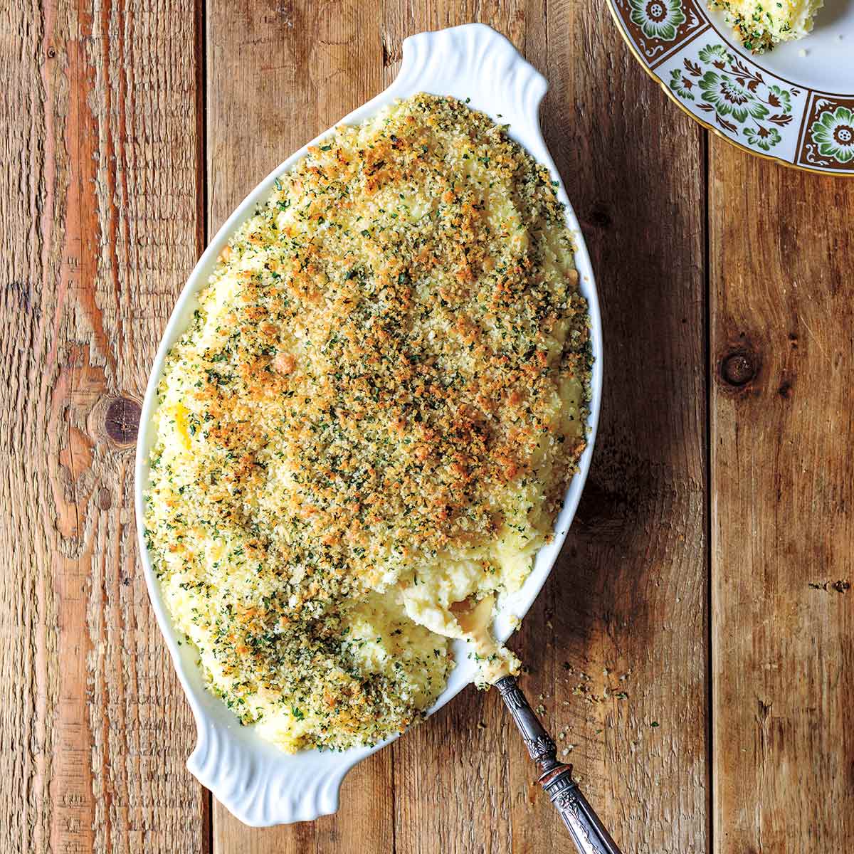 An oval serving dish filled with mashed potato gratin and a portion of it on a plate beside the dish.