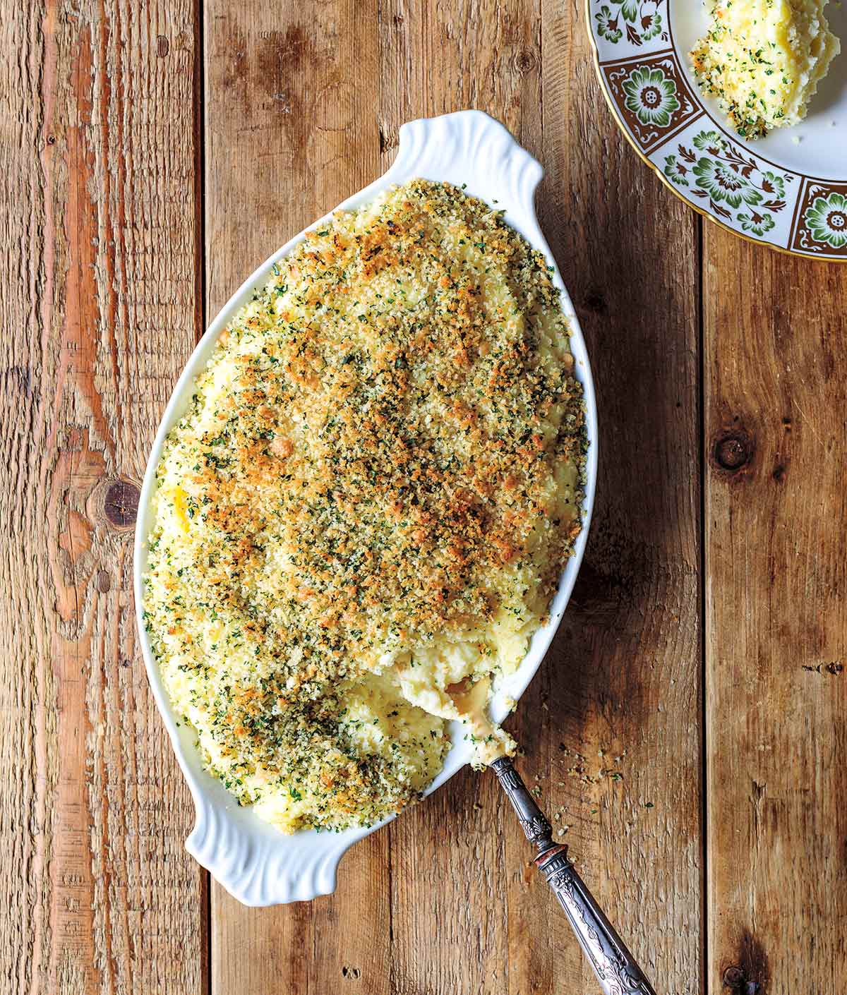 An oval serving dish filled with mashed potato gratin and a portion of it on a plate beside the dish.