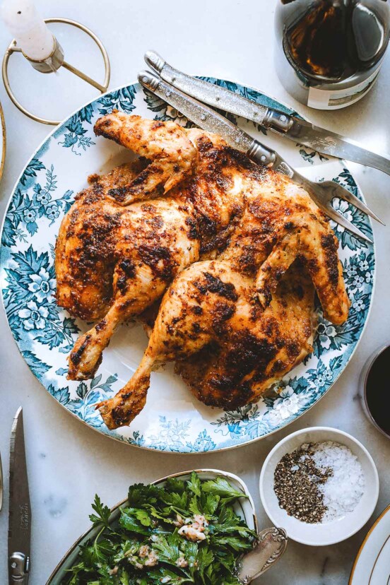 A spatchcocked mayo roast chicken on a blue and white plate with a salad and a bowl of salt and pepper nearby.