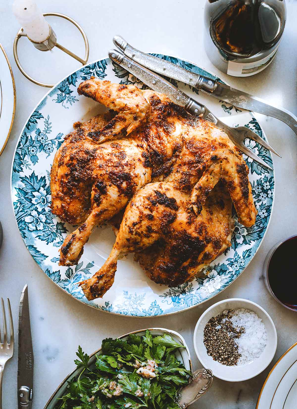 A spatchcocked mayo roast chicken on a blue and white plate with a salad and a bowl of salt and pepper nearby.