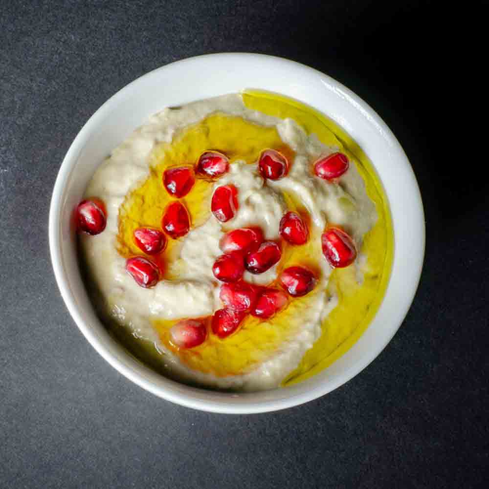 A bowl of moutabal topped with olive oil and garnished with pomegranate seeds.