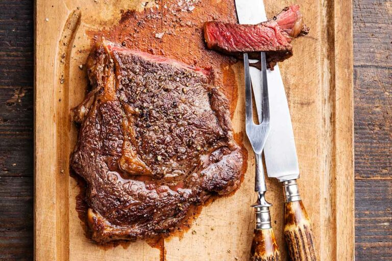 A cutting board with a grilled steak and a carving fork and knife.