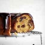 A partially cut orange chocolate chunk cake on a round wire rack.