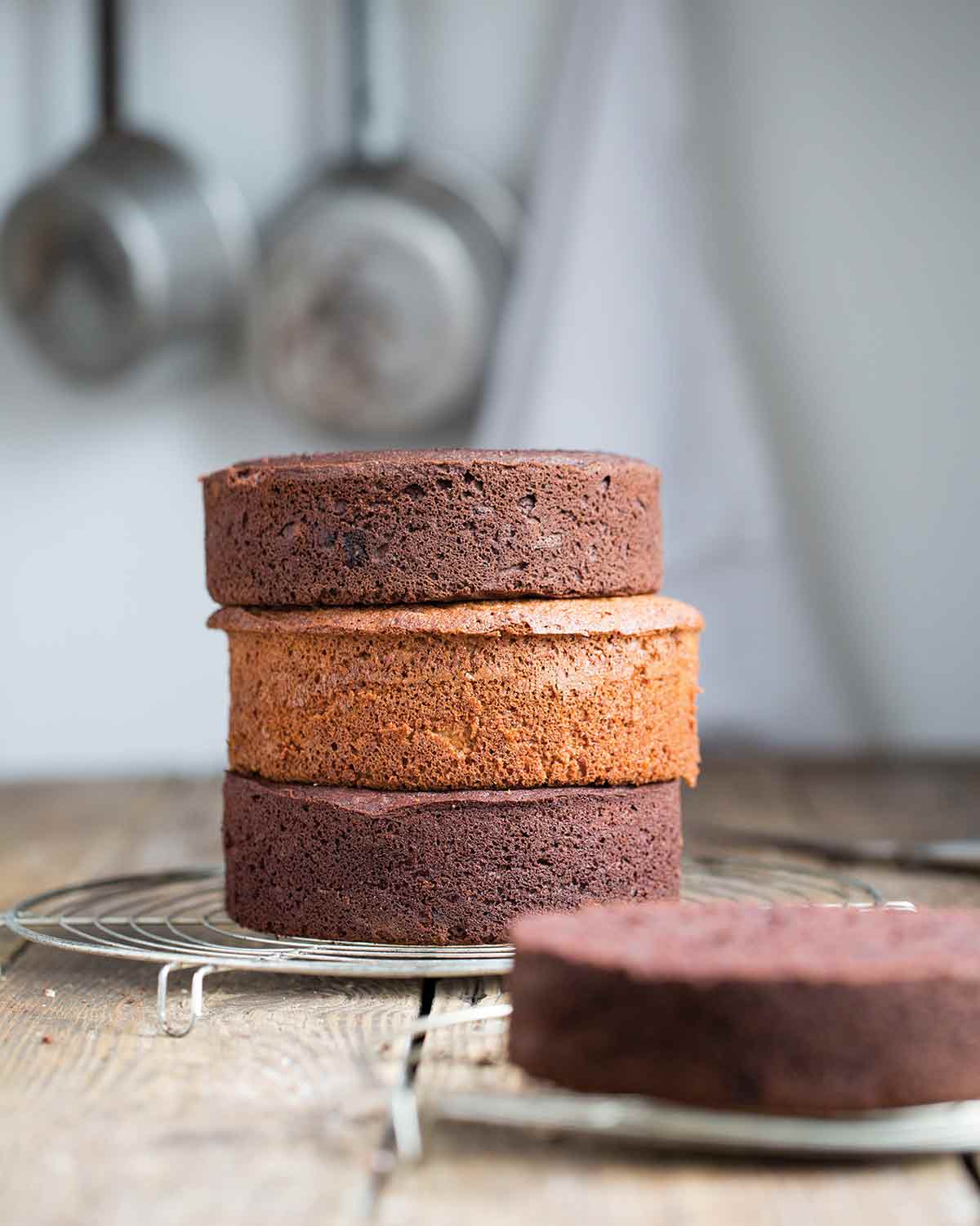 A paleo vanilla cake stacked between two chocolate cakes on a wire rack.